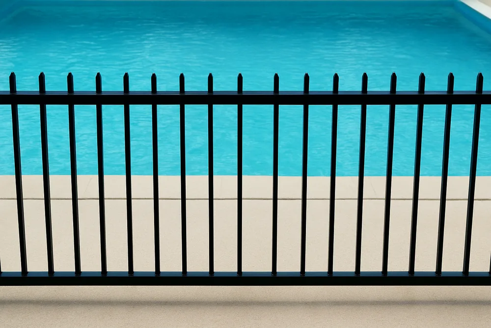 A line of black pool fence palings with the paved edge of a pool beyond — pool fence and safety certificate, Cairns. Illustrative example.